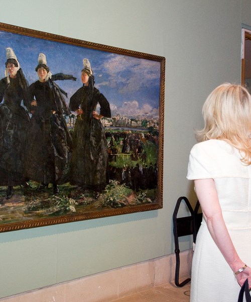 Two people viewing an impressionist painting showing three identically dressed people in old-fashioned black dresses and white hats