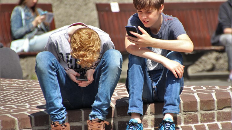Two young kids sit on a step and look at their mobile phones.