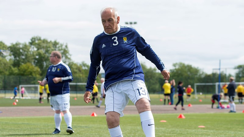 A elderly person playing control the ball while playing Walking Football on an outdoor pitch