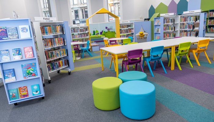 Brightly coloured children's area in Partick Library. There are round stools, coloured chairs, bright carpets and lots of books.
