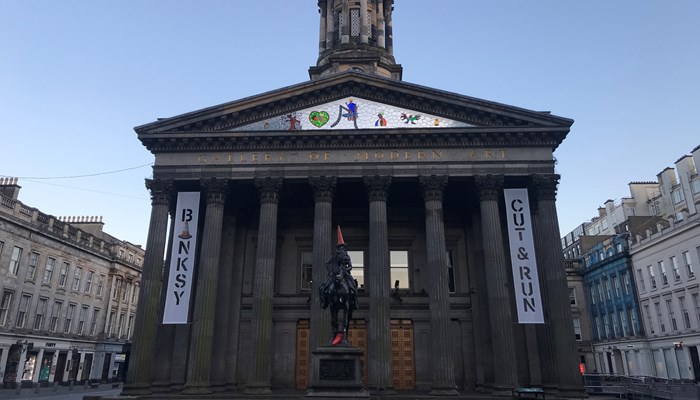 Classical building with columns at the front, decorated with banner advertising Banksy exhibit