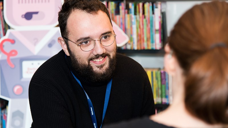 A man facing a women, giving advice and smiling in a library setting