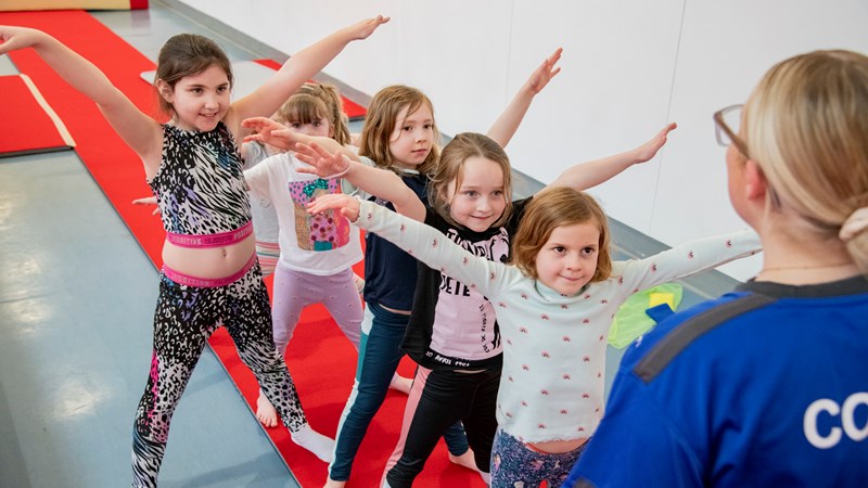 A group of children balancing in a line in front of a gymnastics coach
