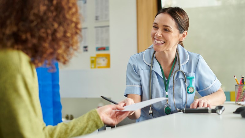 A medical professional hands a piece of paper to a client who is wearing a green jumper.
