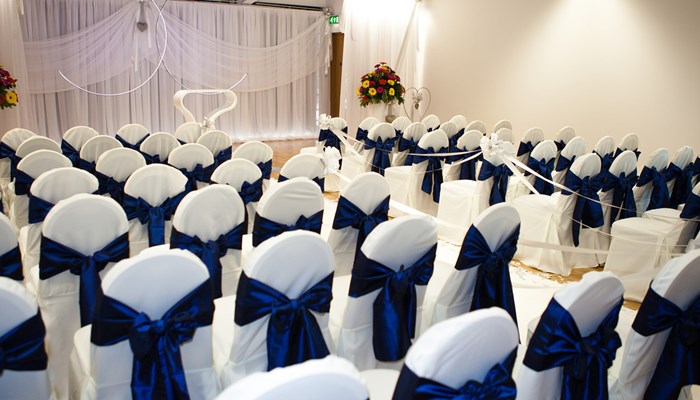 several chairs wrapped in white with a blue row ready for a wedding ceremony. the are all facing the front of the room