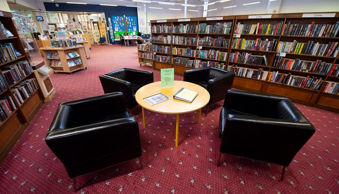 Seating area in Drumchapel Library. There are wooden bookshelves surrounding a table with 4 black leather chairs on a red carpet