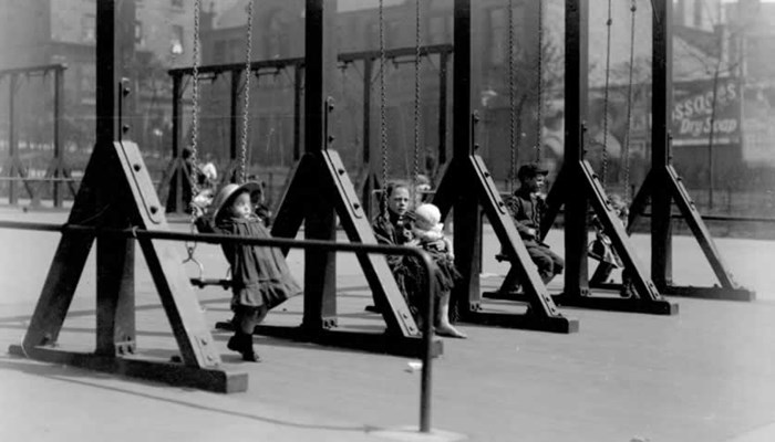 A black and white photo of a swing playground with lots of children swinging on them