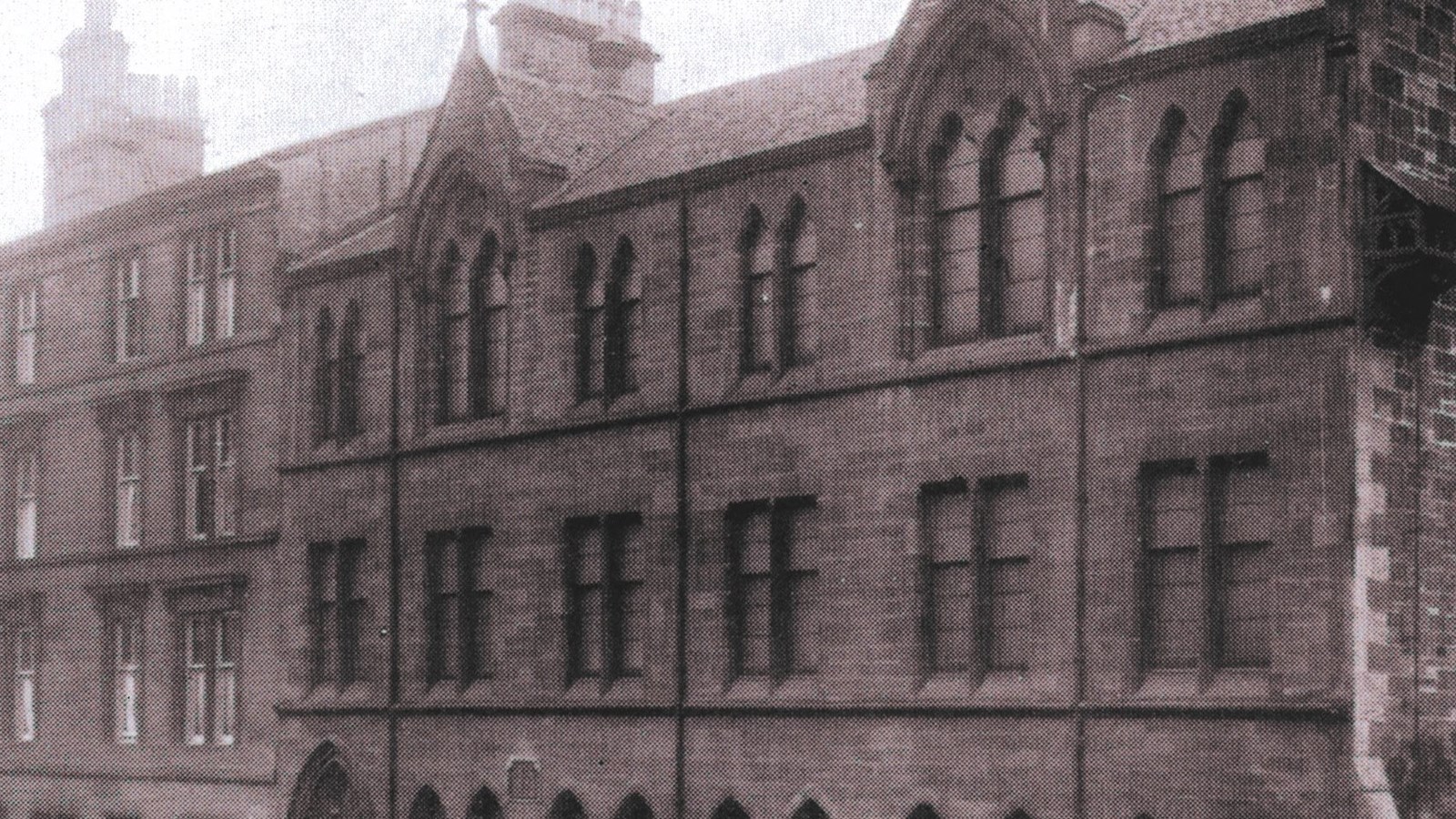 A photograph of a Boys' Brigade large red sandstone building with a slate roof with a black iron gate surrounding it.