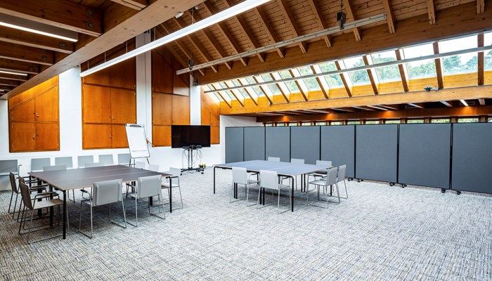 large meeting space with two large tables with chairs round them. the room has windows up high with wooden panelling across the roof