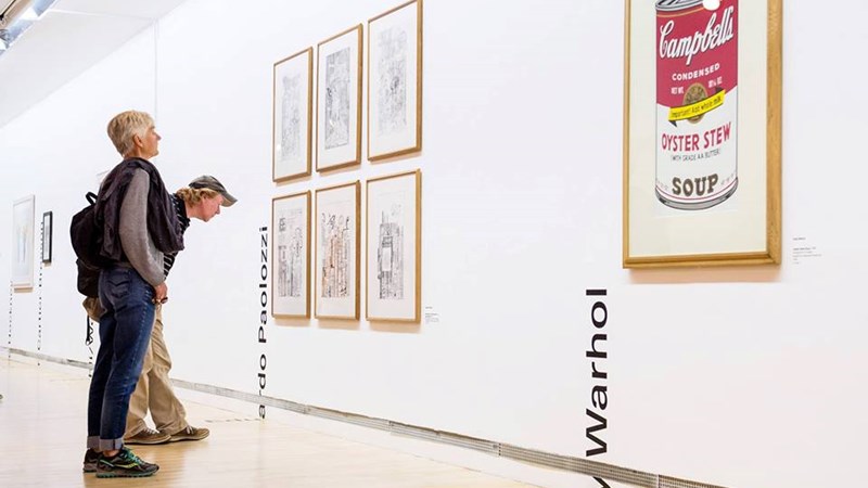 Photograph of two people looking at framed prints on the wall at GoMA