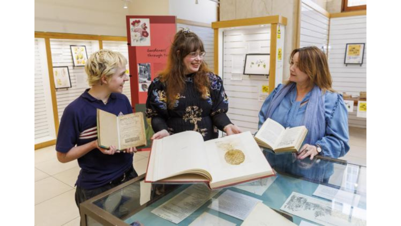 Three people are standing next to a display case holding books, smiling.