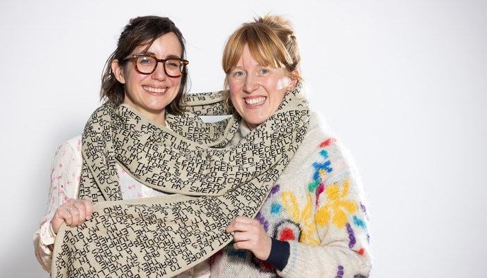 Two women wrapped in a long handmade scarf