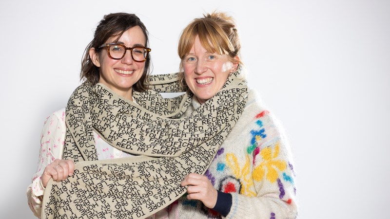 Two women wrapped in a long handmade scarf