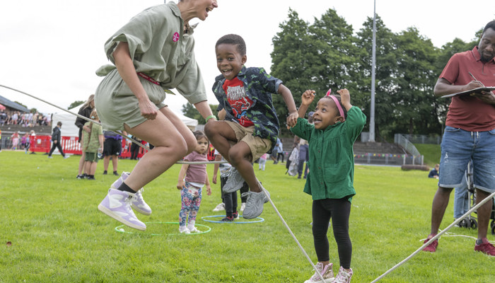 Adult and children skipping rope together on grass at a community outdoor play event.