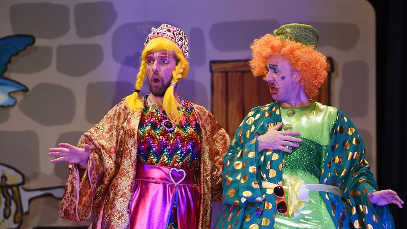 Two men dressed as the Ugly Sisters, one with a blonde plait wig and the other with a red curly wig on, performing in a community pantomime called Cinderella