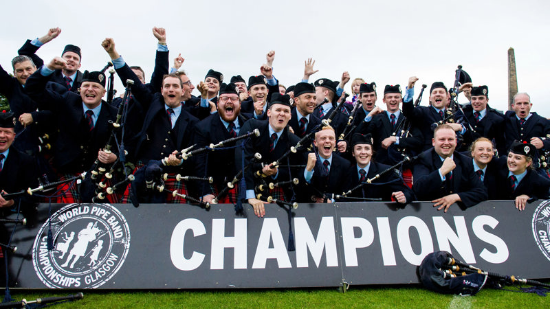 World Pipe Band Champions celebrating behind a sign that reads "Champions" 