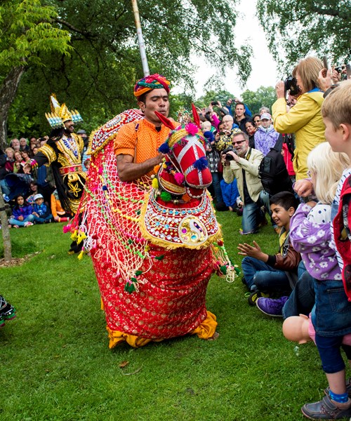 Children watching brightly coloured performers at Glasgow Mela
