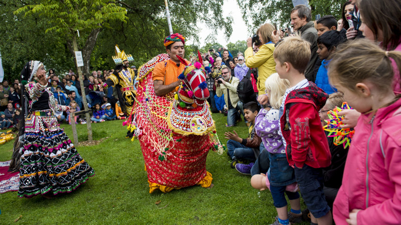 Children watching brightly coloured performers at Glasgow Mela with other members of the crowd taking photographs.