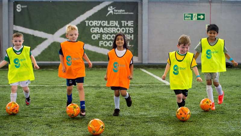 Children playing football wearing brightly coloured vests