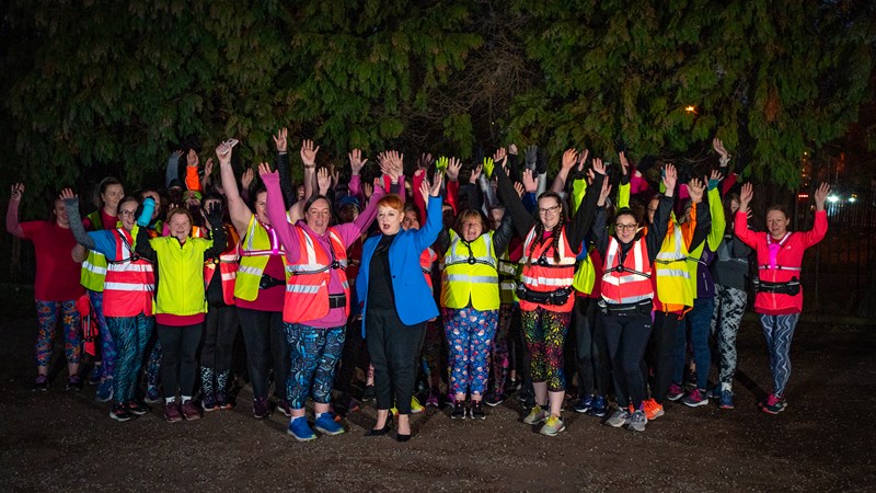 A group of joggers together smiling with their hands in the air while wearing reflective running gear