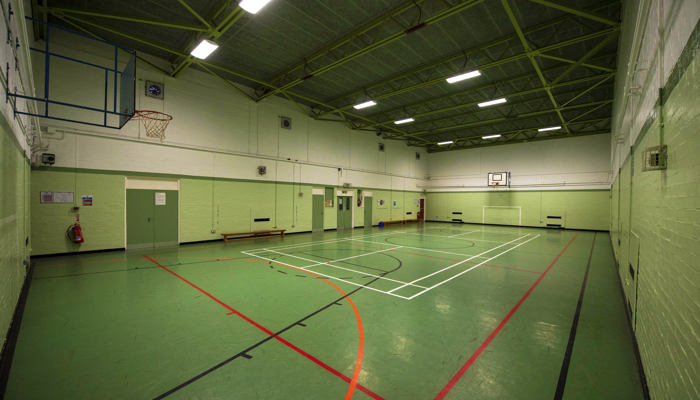 games hall which is marked out for different games. the floor is marked in green with white, black and red lines for the games. the walls are painted light green. there is a basketball net on the far wall