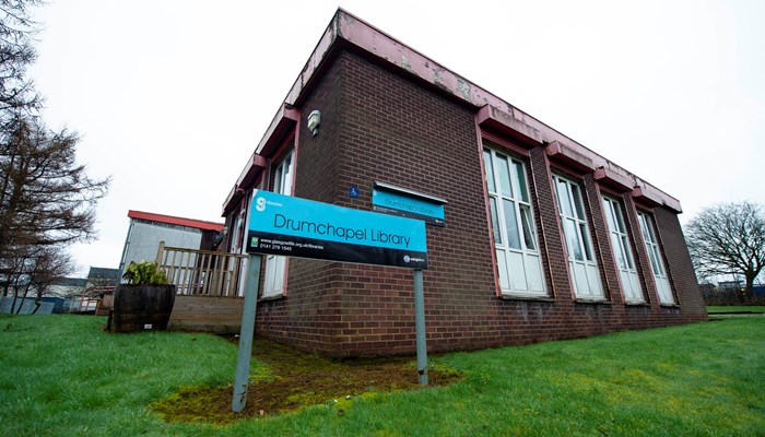Exterior of Drumchapel Library which is a brown brick flat-roofed building with tall rectangular white windows. There is also a black and blue library sign near the entrance