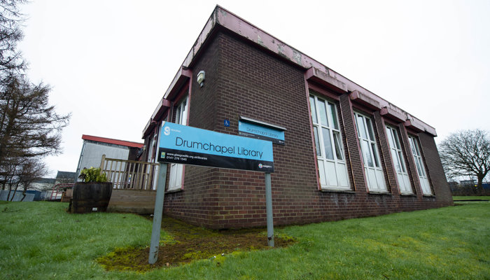 Exterior of Drumchapel Library which is a brown brick flat-roofed building with tall rectangular white windows. There is also a black and blue library sign near the entrance