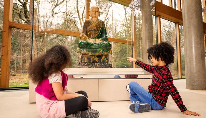 Two children sitting on the floor in the Burrell Collection looking and pointing at a statue which is part of the collection