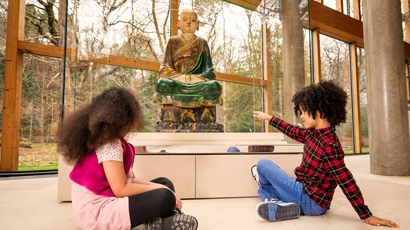 Two children sitting on the floor in the Burrell Collection looking and pointing at a statue which is part of the collection