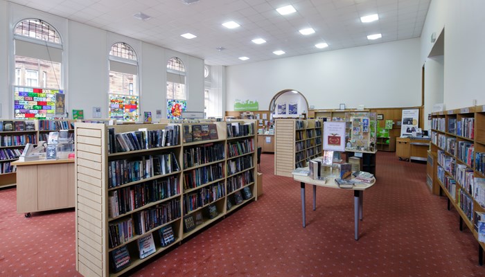 A full bookcase in a library. The floor has red carpet and there are white walls and tall windows in the background.