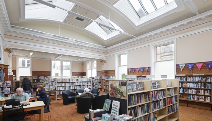 An interior shot of Pollokshields Library with people sitting on chairs and working at tables.