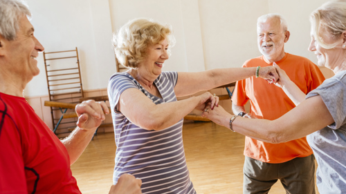 A group of older people taking part in a dance class all standing in a circle looking at each other
