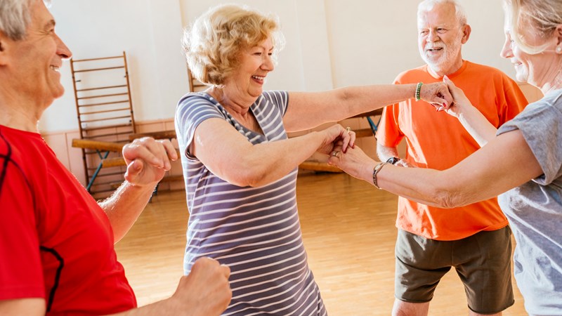 A group of older people taking part in a dance class all standing in a circle looking at each other