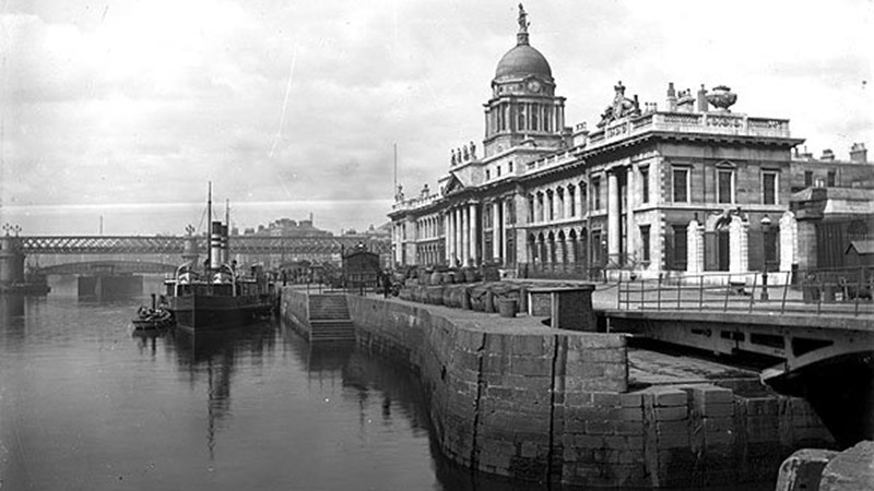 A black and white photo of a river with a building in the right hand side of the photo. Building is known to be Custom House in Dublin.
