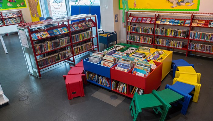 Brightly coloured children's section of Gorbals Library. Lots of boxes filled with picture books and red, yellow, blue and green coloured chairs.