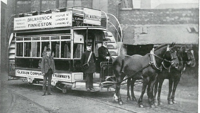 Three men stand nearby a horse drawn tram with Glasgow Corporation Tramways written on the side. 