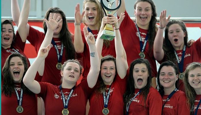 A group of people celebrating winning a sports competition with medals round their neck and one holding a trophy above their head