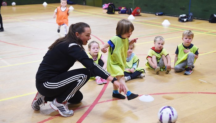 A football coaching helping a child kick a football during an indoor session