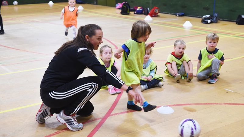 A football coaching helping a child kick a football during an indoor session
