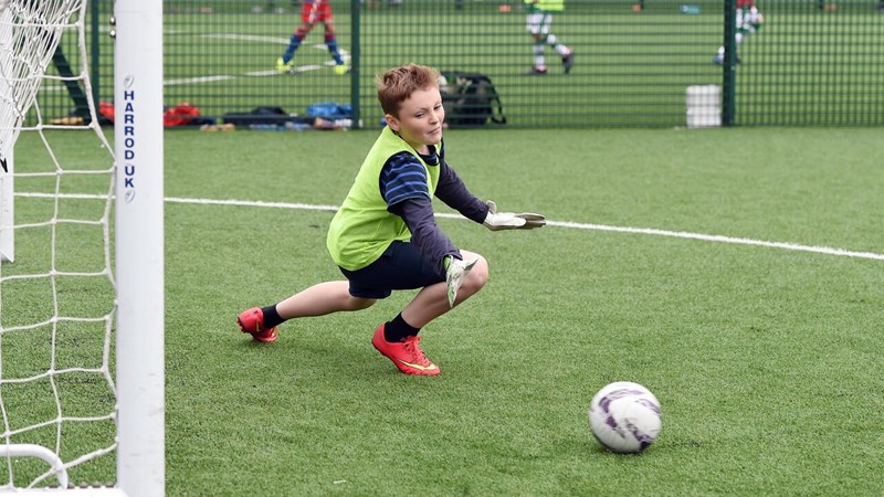A young person diving to save the ball while playing as goalkeeper