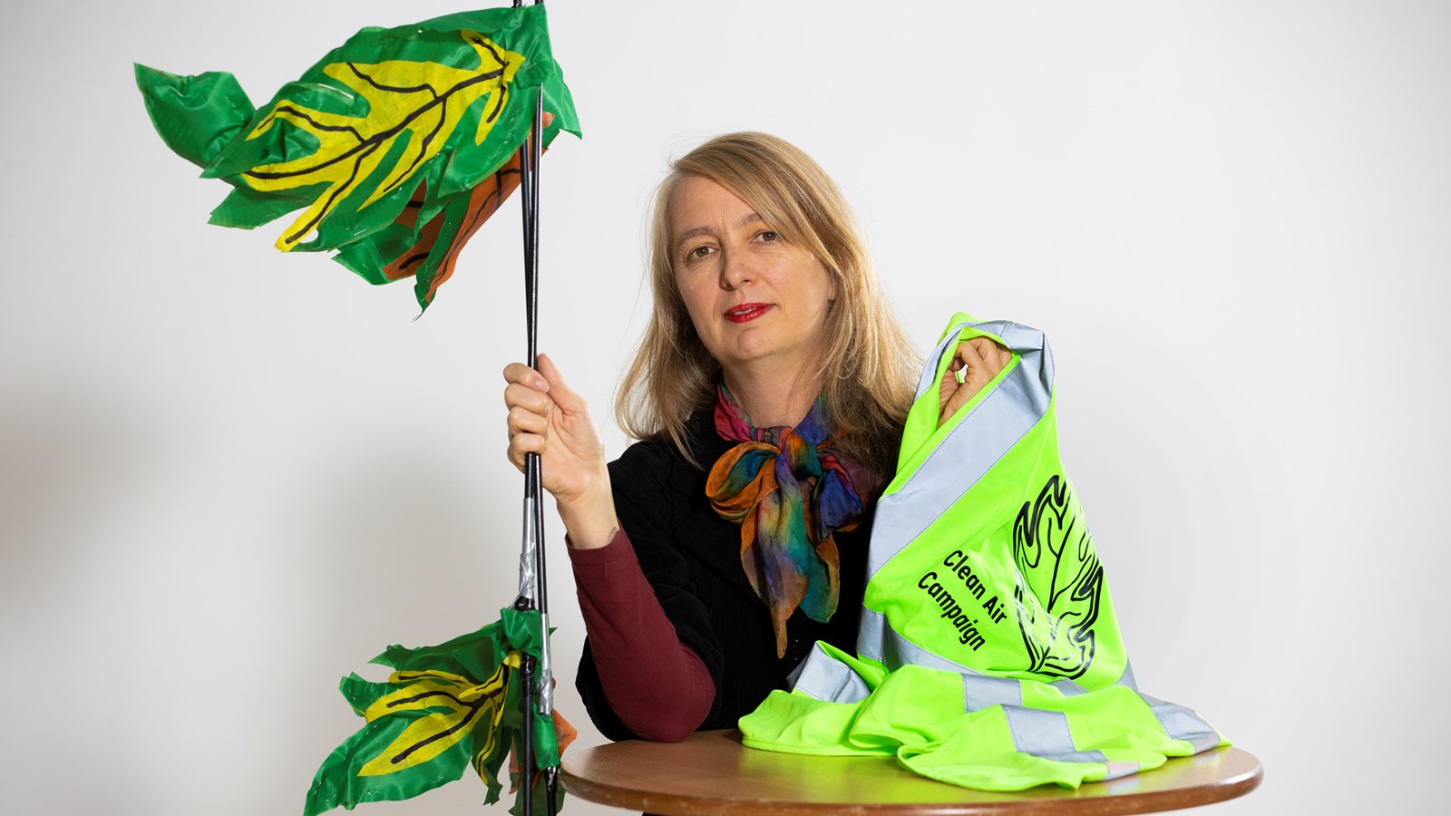 Artist Zoe Walker poses with a high vis waistcoat and leaf prop