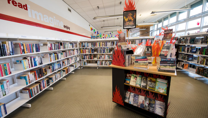 A large selection of bookshelves. There is wall writing on the left hand wall that reads 'Read, Imagine, Enjoy'