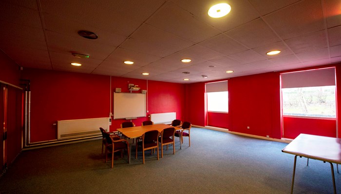 A table and chairs set up for a meeting in a room with red walls.