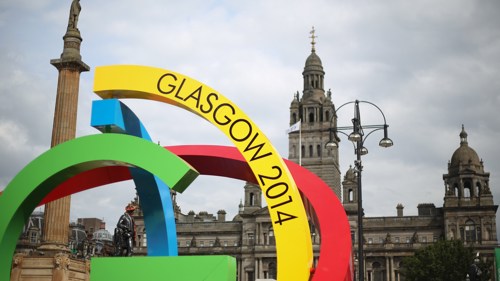 A large colourful sculpture in a city centre square. It is made up of large arches and circles and has text Glasgow 2014 on it.