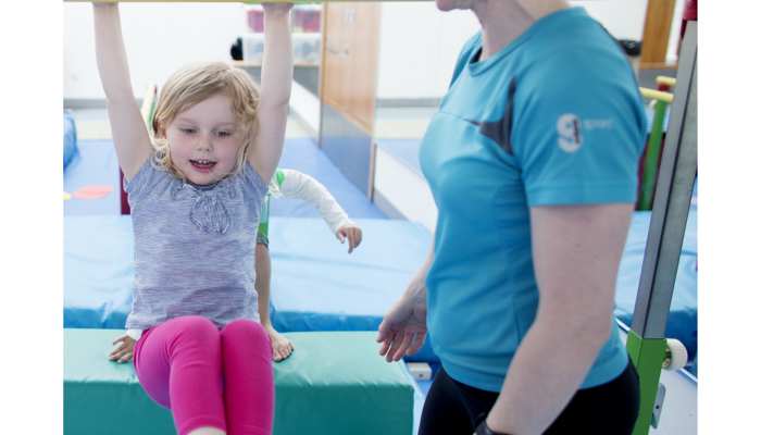Little girl swinging on bar next to instructor 
