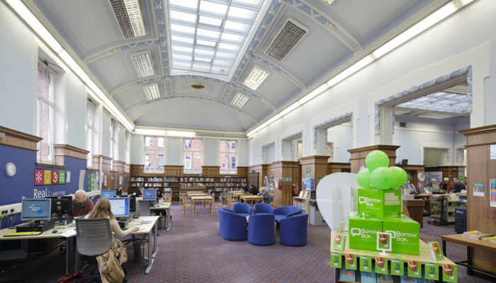 The PC area of the library which also has a table and soft blue chairs for reading or for meeting groups. The high ceiling is curves and has a long, grid, colonial-style skylight.