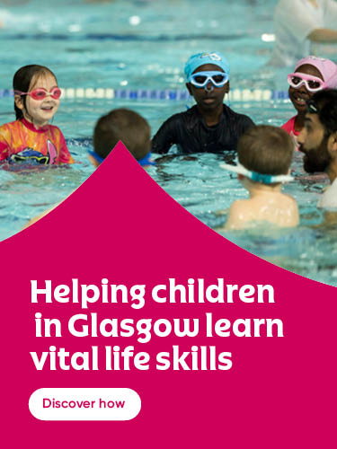 Children wearing swimming goggles take part in a swimming lesson in an indoor pool.