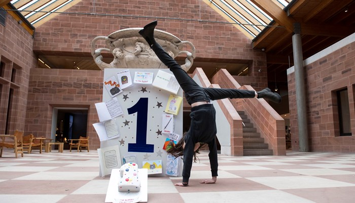 Mia cartwheels in front of giant first anniversary card at Burrell Collection