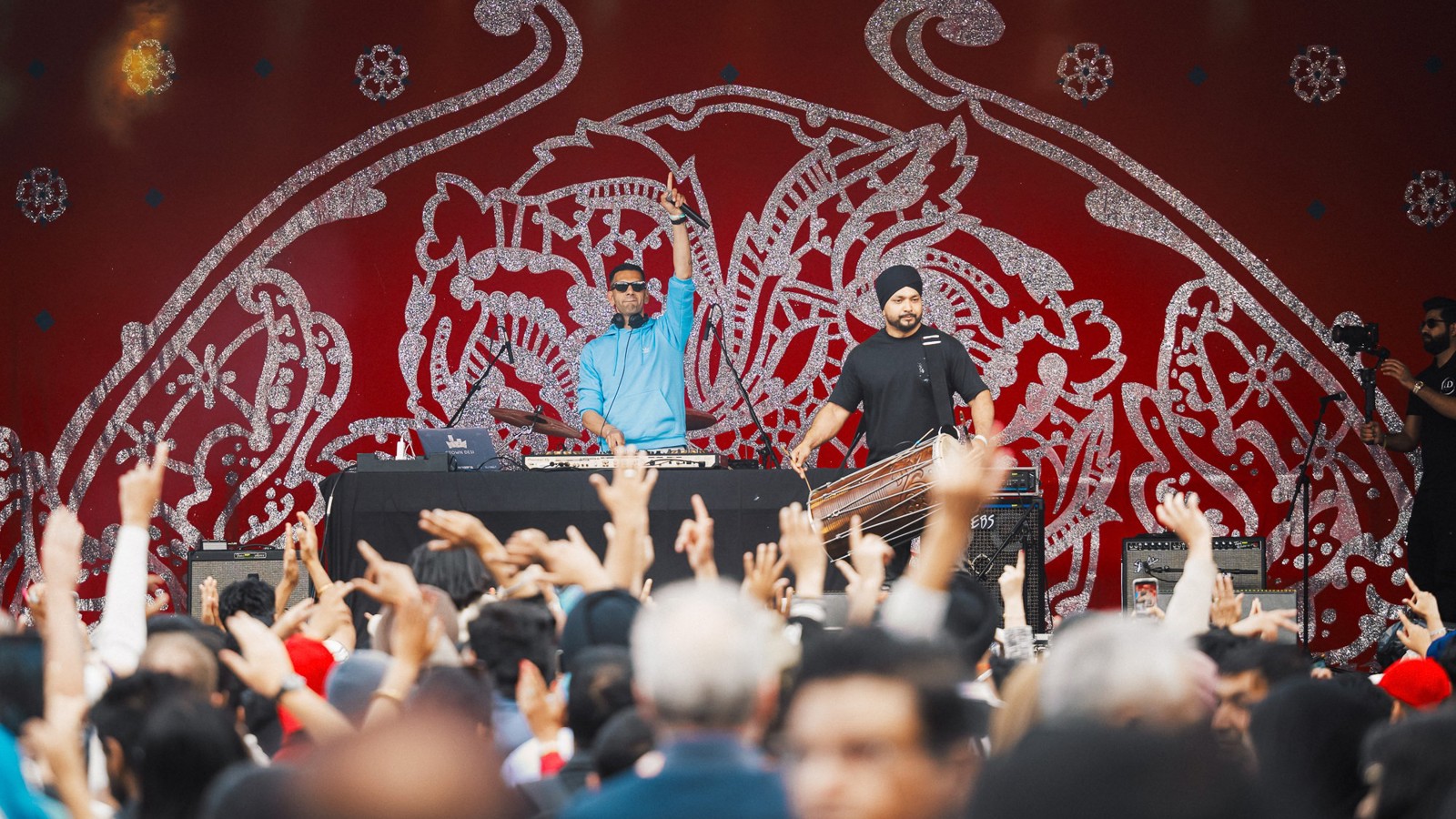 Musicians perform in front of a large crowd waving their hands in the air