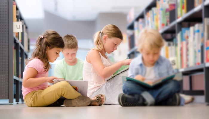 Four children sitting on the floor in a library reading books